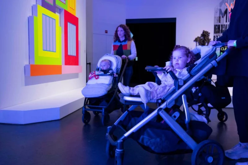 Two babies in strollers being pushed through an art gallery