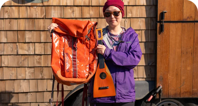 A person holds a Black Hole backpack and a ukulele.