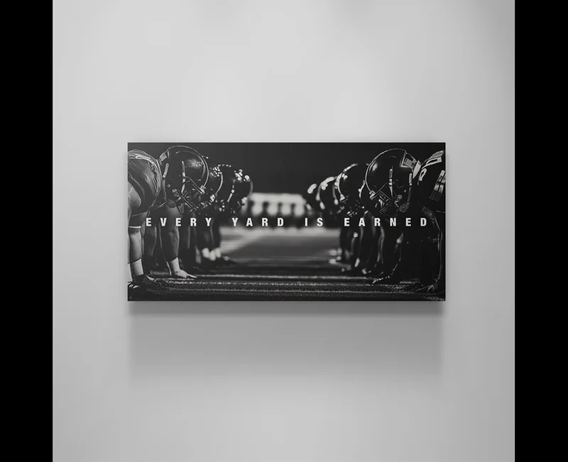 Black and white artwork of two opposing football teams lined up at the line of scrimmage, facing each other in a tense standoff. Bold text across the center reads ‘EVERY YARD IS EARNED.’ Black and white artwork of two opposing football teams lined up at the line of scrimmage, facing each other in a tense standoff. Bold text across the center reads ‘EVERY YARD IS EARNED.’