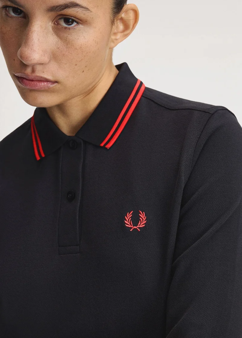 A female model wearing a twin tipped long sleeved Fred Perry Shirt in Black / Flamingo Tan / Flamingo Tan