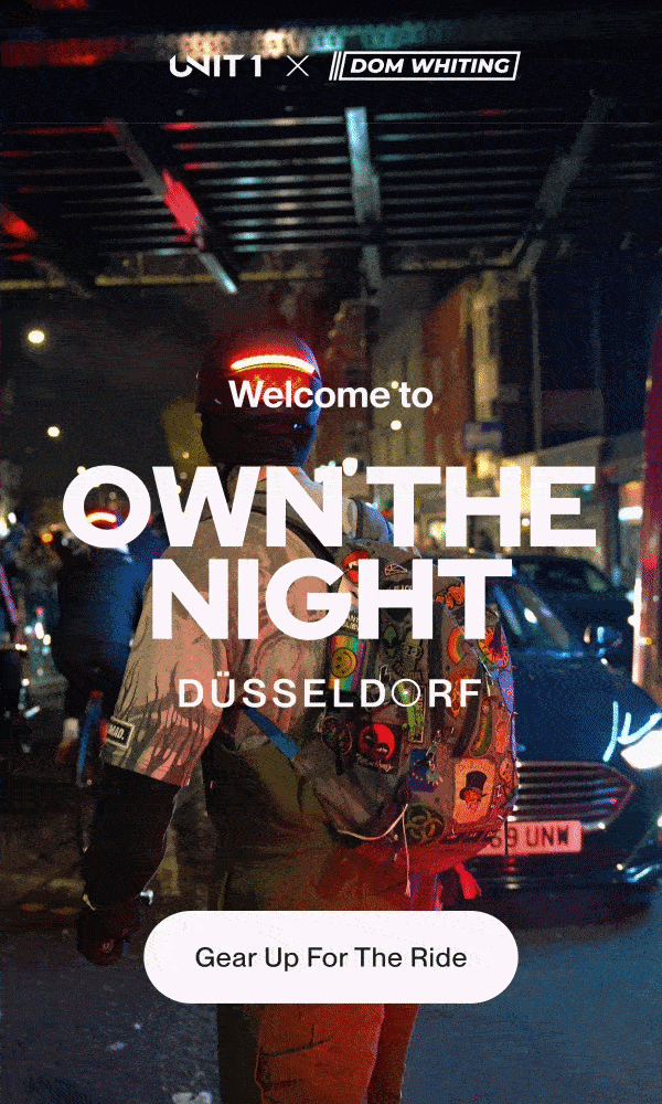 Night street scene with cyclist wearing a glowing helmet, featuring UNIT 1 x Dom Whiting branding, “Welcome to OWN THE NIGHT DÜSSELDORF,” and a “Gear Up For The Ride” button.