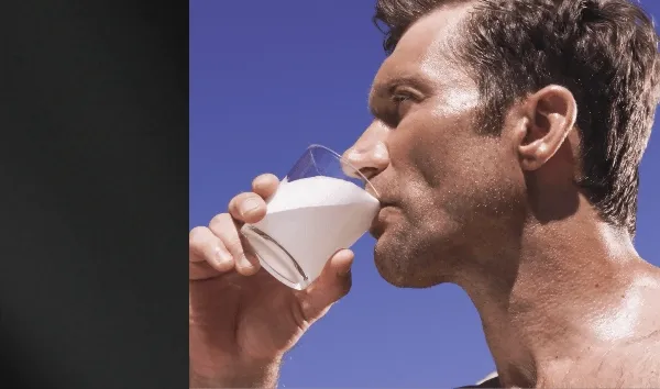 Athlete drinking a glass of ARMRA Colostrum outdoors under a clear blue sky.