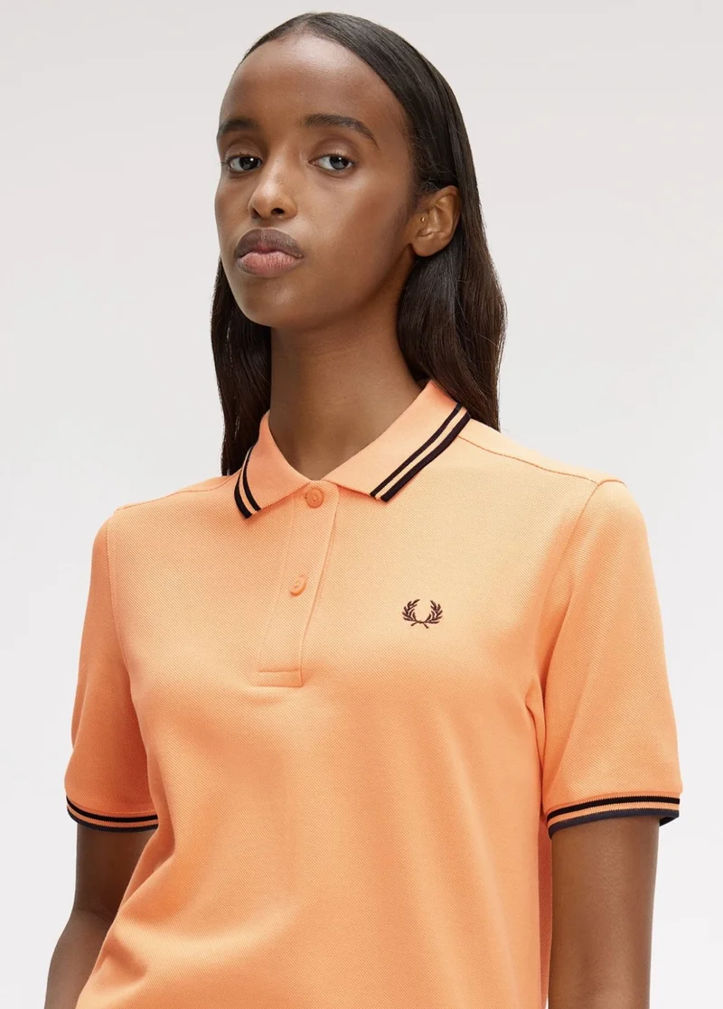 A female model wearing a Fred Perry Shirt in a vibrant peach colour with black twin tipping on the collar