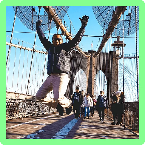 Image description: A traveler jumping in the air for a photo on the iconic Brooklyn Bridge