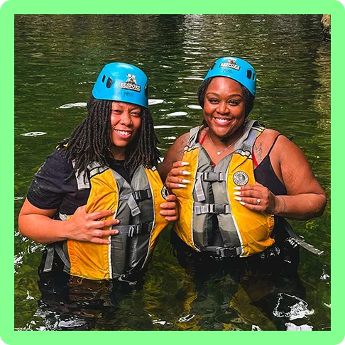 Image description: Two travelers smiling in the water with their lifejackets and helmets on for a water activity in Puerto Rico