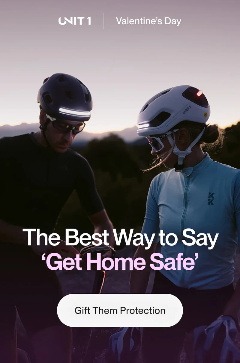 Two cyclists at dusk wearing UNIT 1 helmets with integrated lights, with text ‘The Best Way to Say Get Home Safe’ and a button ‘Gift Them Protection’.