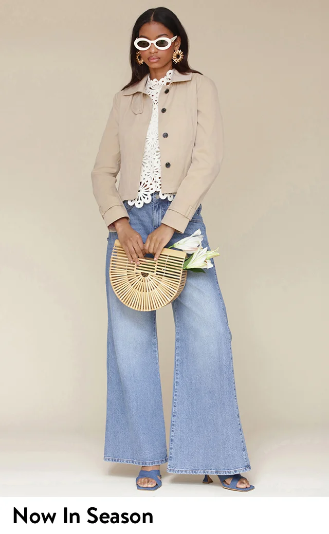 A woman wearing a tan jacket with a lacy white top and wide-leg jeans.