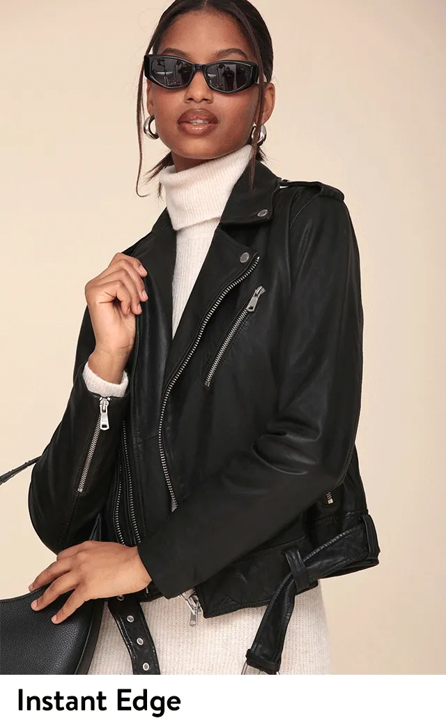 A woman wearing a black leather jacket over a white turtleneck sweater dress.