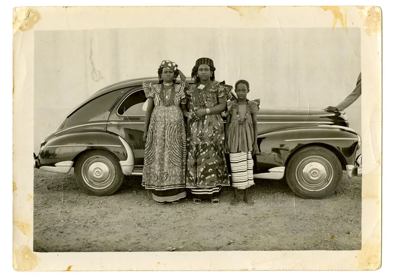 A sepia-toned photograph of three people in front of a car