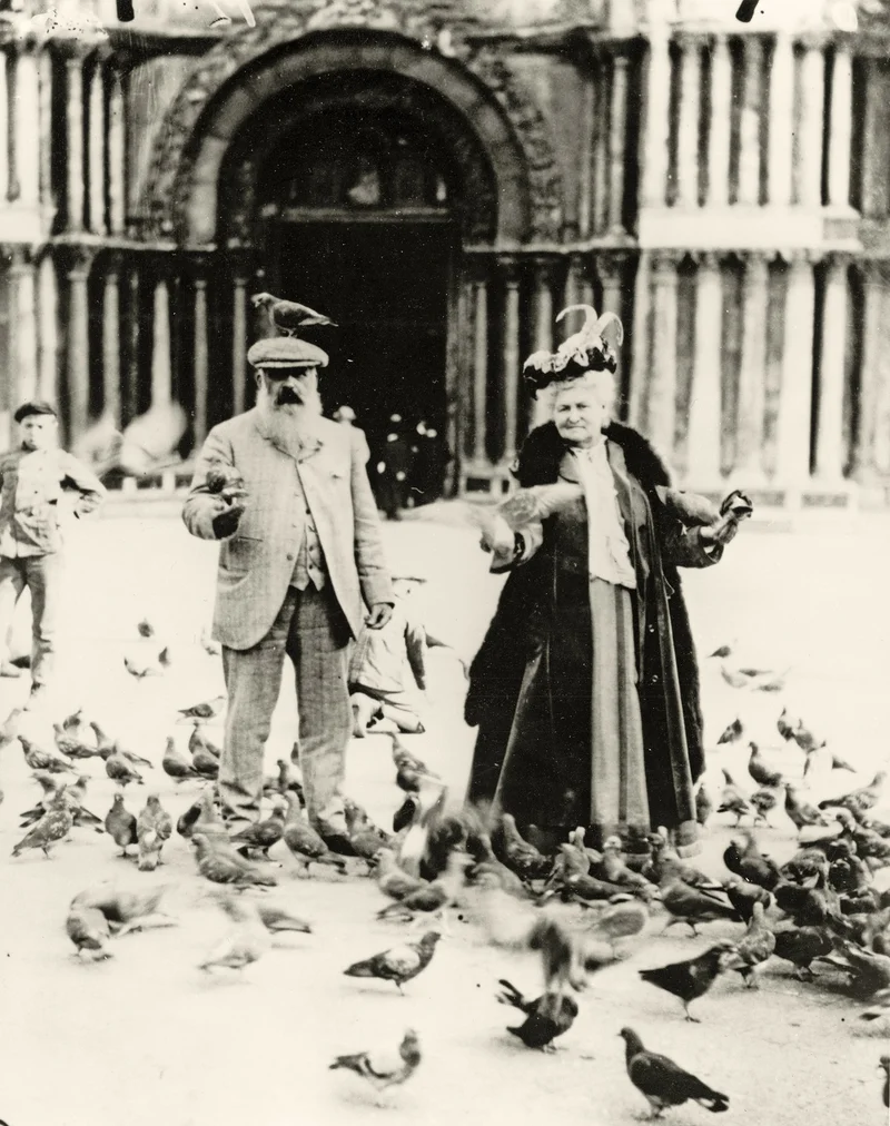 Black-and-white photograph of a man and woman feeding pigeons