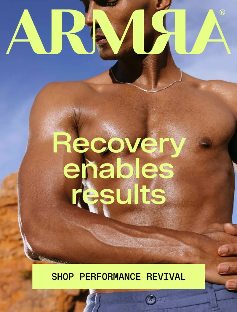 Recovery enables results - SHOP PERFORMANCE REVIVAL. Shirtless athletic man outdoors against blue sky and red rock landscape, wearing a thin necklace, arms crossed over chest.