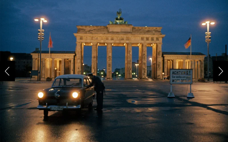 A car in front of the great gate in East Berlin in 1961. A sign reads, 'Attention! You are now leaving West Berlin.”