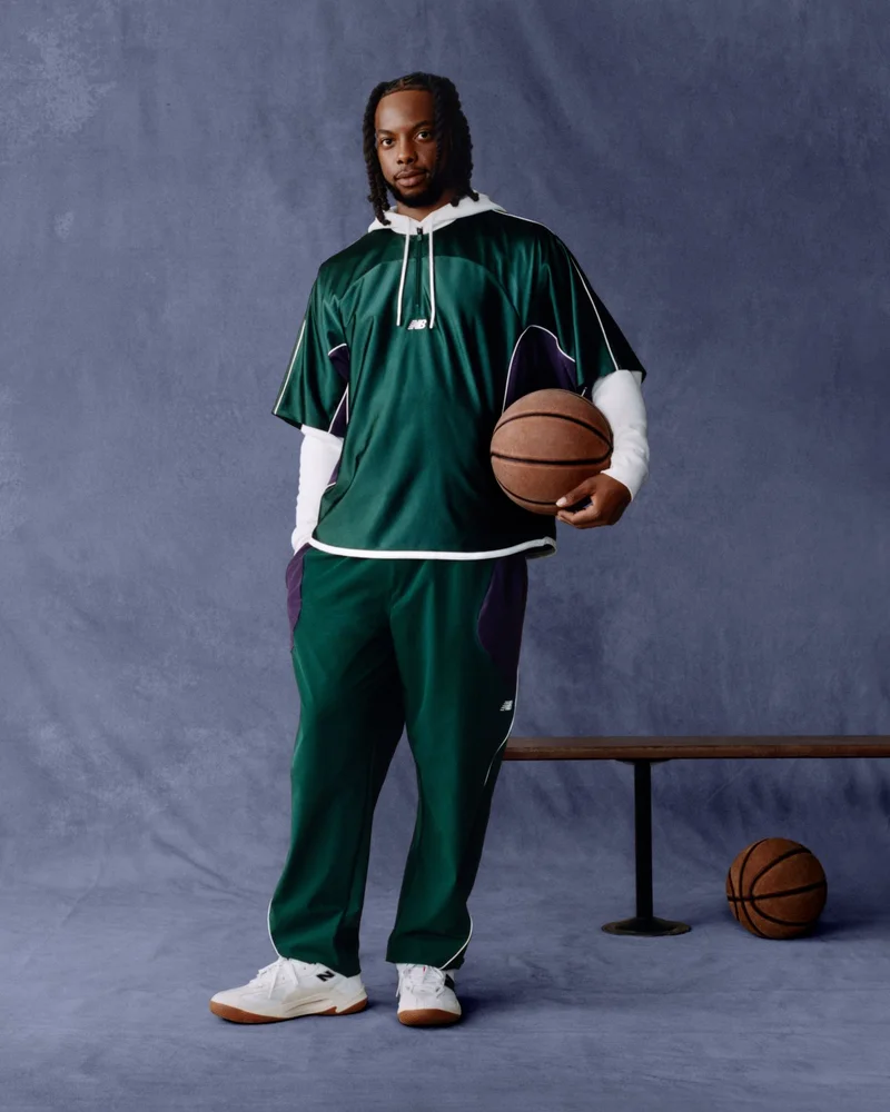 A man in a dark green track suit holding a basketball.