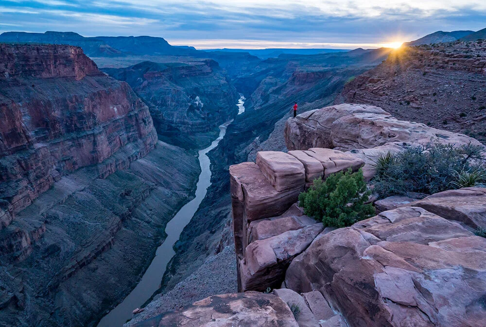 A hiker takes in the view of the Colorado River winding its way through the Grand Canyon at sunset.