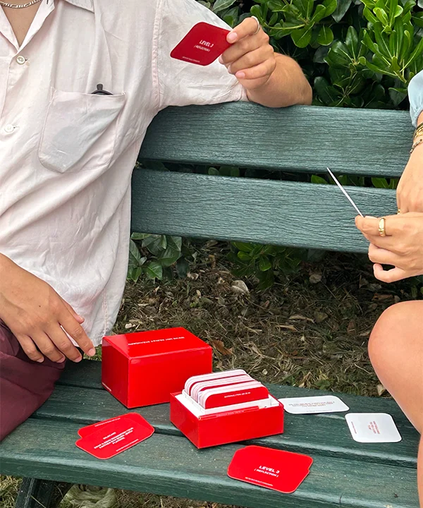 image of someone sitting on a green park bench playing the We're Not Really Strangers Card Game with someone else.