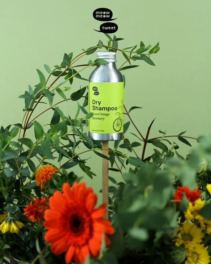 A metal bottle with a green label is propped on a stick amidst flowers