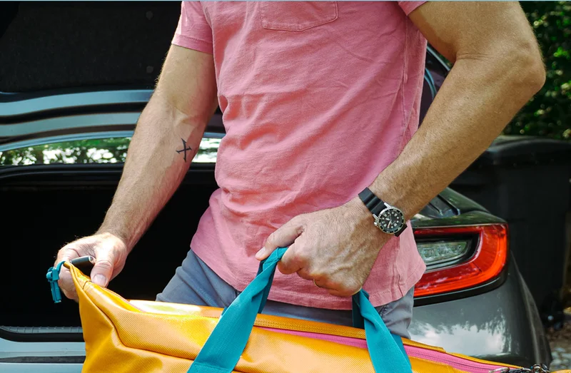 Person wearing Promaster Dive 35mm, carrying a bag by a car.