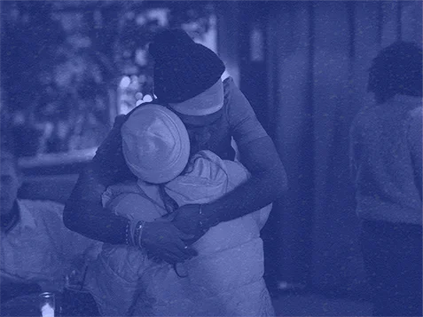 Two people embrace in a warm hug, set against a calm, indoor backdrop.