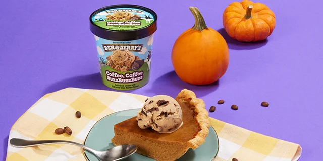 A pint of Ben & Jerry's Coffee, Coffee BuzzBuzzBuzz ice cream sits on a blue background next to a slice of pumpkin pie.