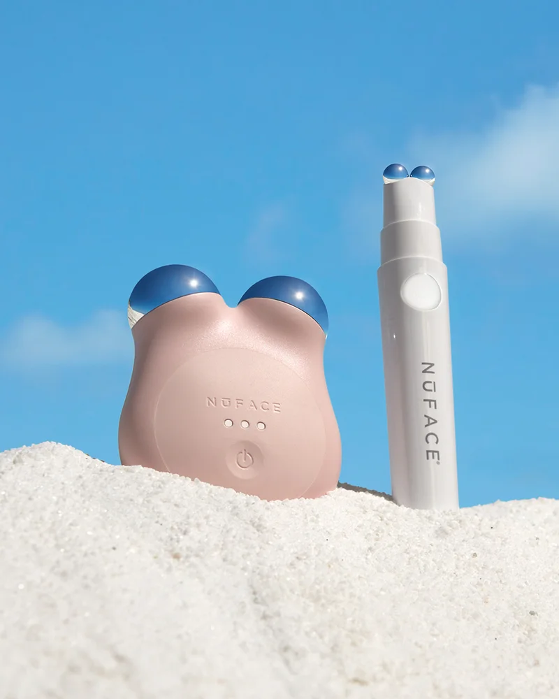 MINI+ in Sandy Rose next to NuFACE  FIX in the sand against a bright blue sky