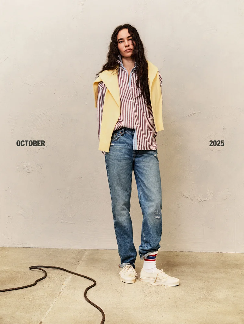 Person wearing a striped button up shirt with a yellow sweater draped over shoulders