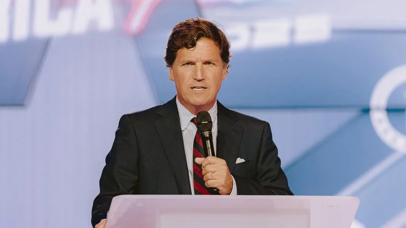 Image may contain: Tucker Carlson, Electrical Device, Microphone, People, Person, Crowd, Accessories, Formal Wear, and Tie