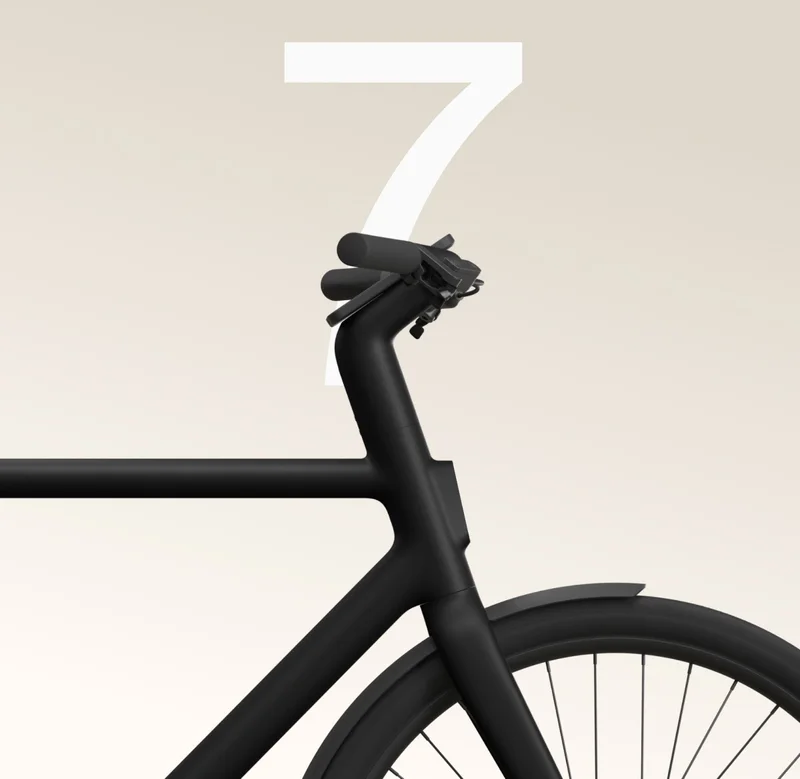 Close-up of the front frame and handlebars of a black Cowboy bike, with a minimalist design and a large white number “7” in the background.