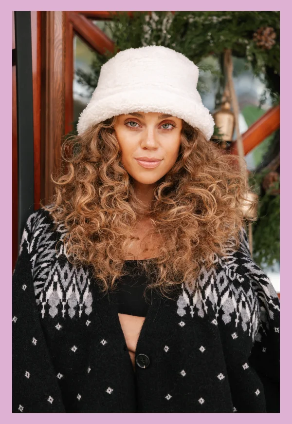 woman with curly hair wearing fluffy bucket hat and black fair isle sweater