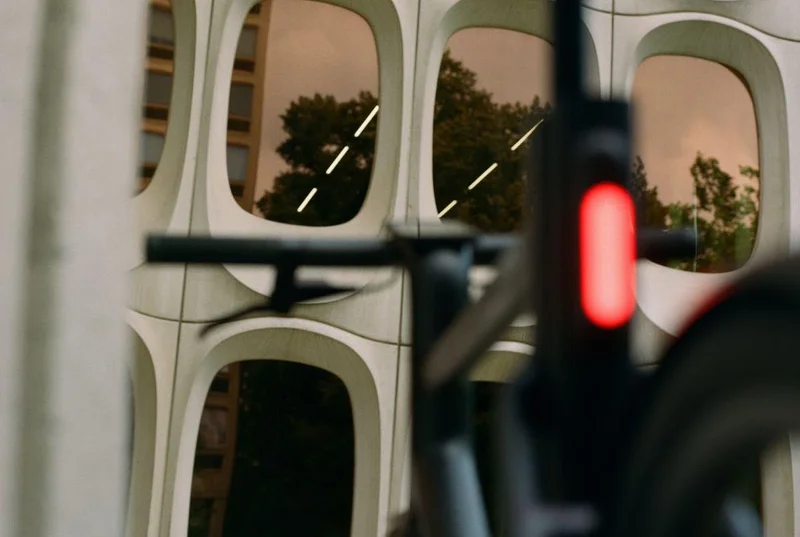 A Cowboy bike, seen from behind and out of focus, against a view of concrete-framed reflective windows