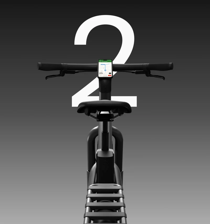 Front view of a Cowboy bike showcasing its sleek handlebars, integrated smartphone mount displaying navigation, and a minimalist rear luggage rack. The number “2” is prominently displayed in white against a dark gradient background.