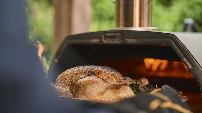 A whole roasted chicken coming out of Ooni Karu 2 Pro