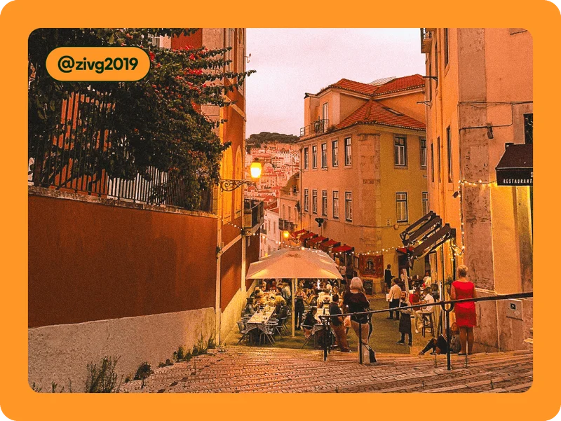 Image description: Cobblestone stairs down to a plaza with an outdoor cafe and string lights, photo taken by @zivg2019