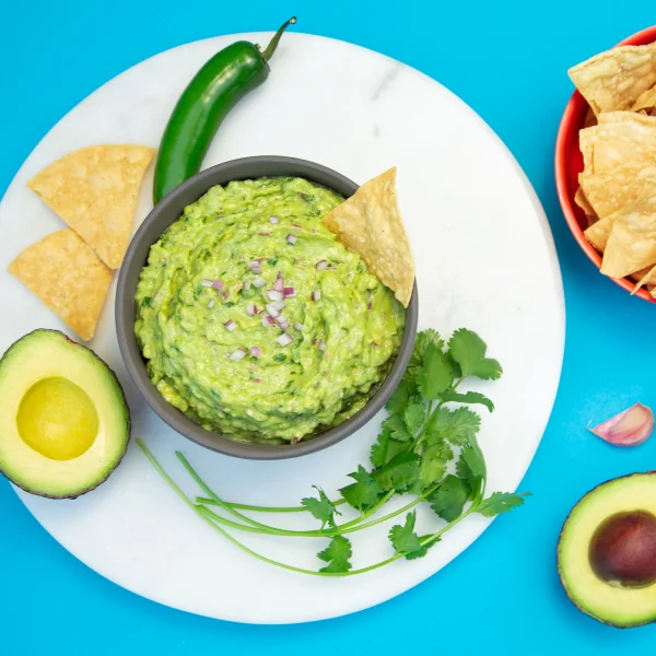 Guacamole in a bowl next to chips, fruits and vegetables