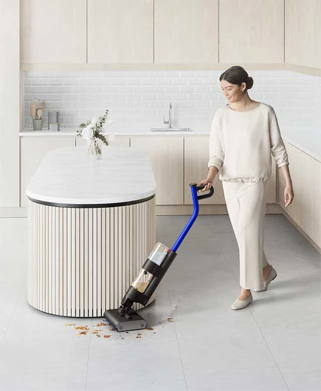 A woman uses the Dyson WashG1 wet cleaner to clean debris on a kitchen floor