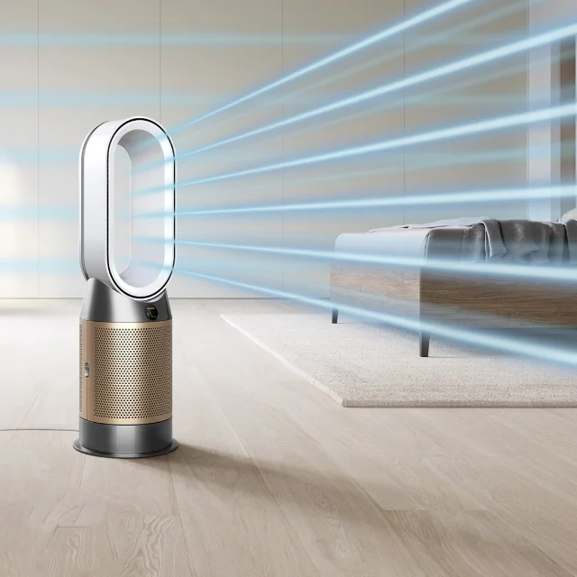 A bedroom setting with a Dyson air purifier is in the foreground emitting a stream of purified air
