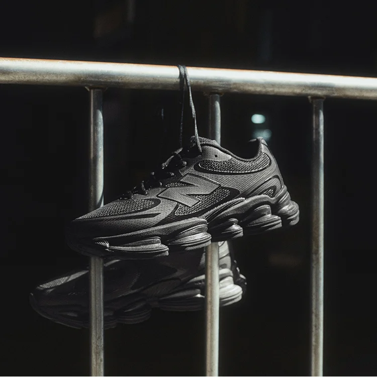 Dark New Balance shoes hanging by their shoelaces from a metal railing.