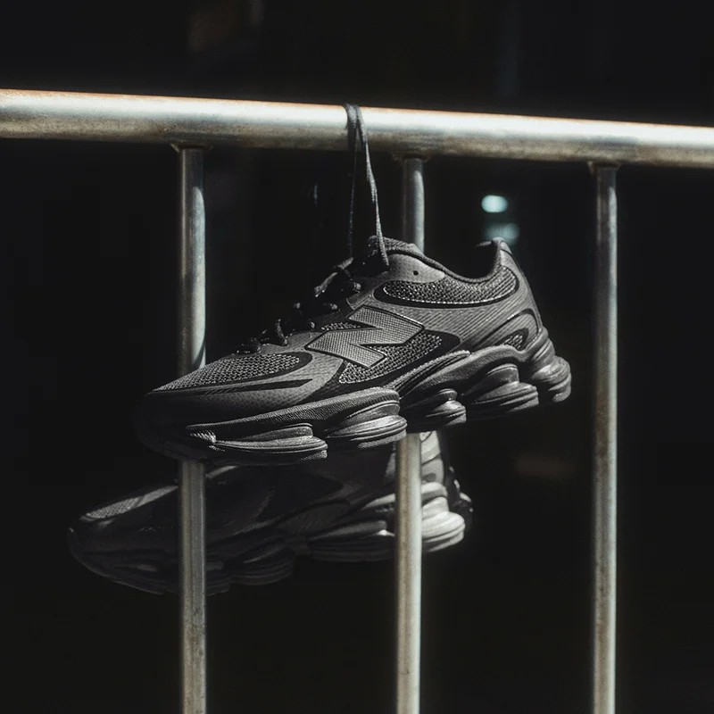 Dark New Balance shoes hanging by their shoelaces from a metal railing.