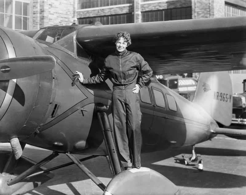 Black and white photo of Amelia Earhart with her airplane.