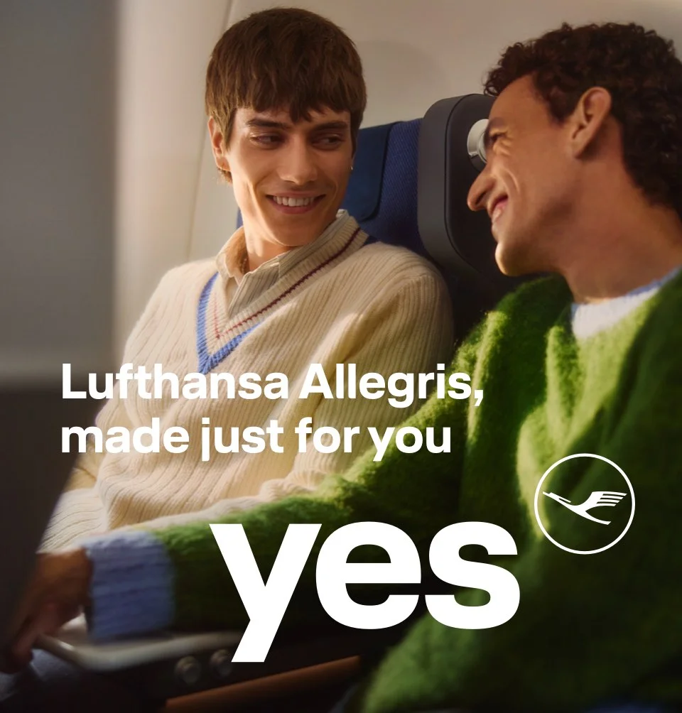 Two young men sitting in premium economy class smile at each other.