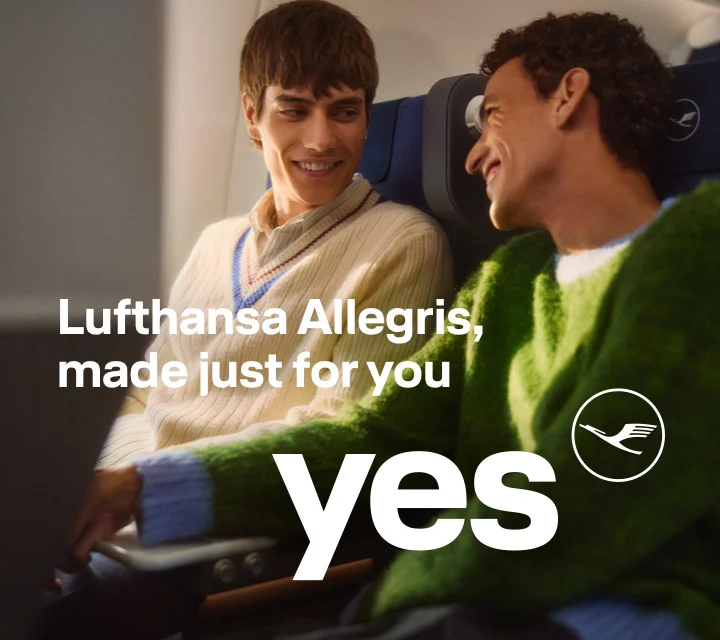 Two young men sitting in premium economy class smile at each other.