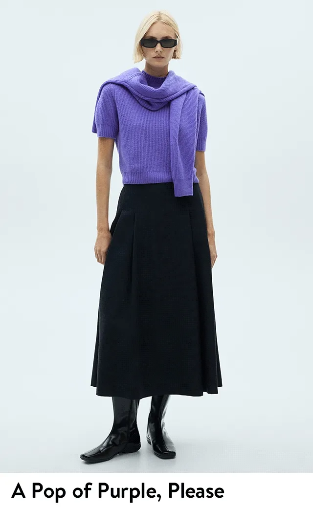 A woman wearing a purple sweater and black skirt.