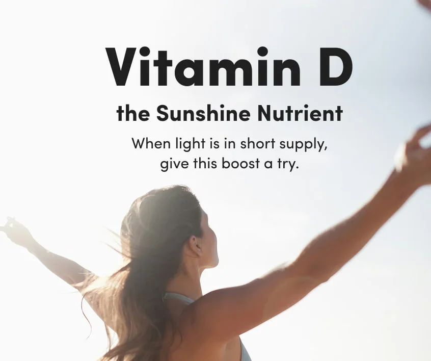 Woman with arms outstretched toward bright sunlight, viewed from behind against a clear sky.