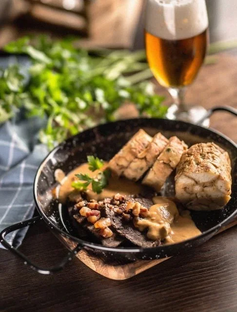 Image Description: A pan of Svíčková (beef tenderloin with cream sauce) served with a glass of beer