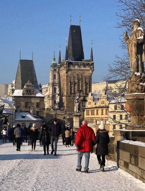 Image Description: Travelers walking along the snow-covered Charles Bridge against the striking backdrop of the Old Town Bridge Tower