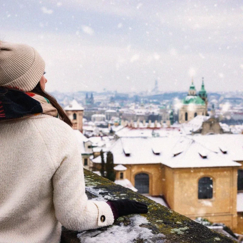 Image Description: A female traveler on top of a tower overlooking Prague’s snow-covered skyline