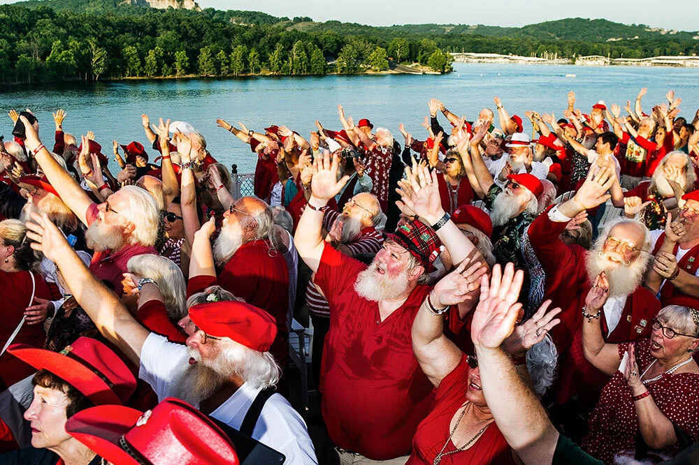 A crowd of Santa lookalikes raise their hands near a body of water