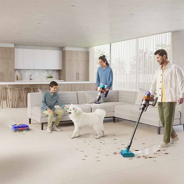 Three Dyson floorcare products in use in a living room as a family cleans up after their dog