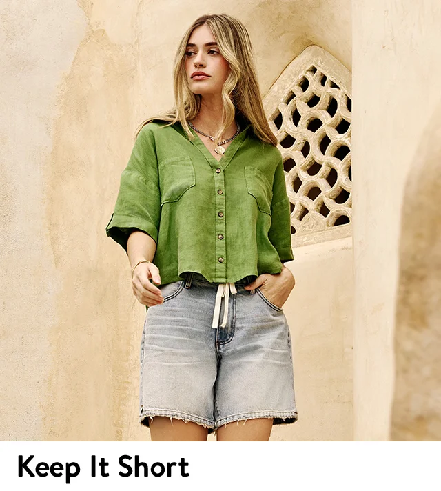 A woman wearing jean shorts and a green short-sleeve button-up shirt.