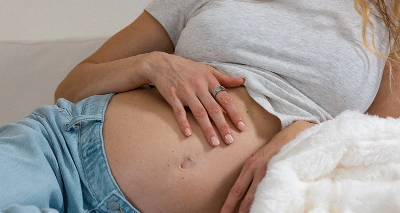 Person with hand over pregnancy belly wearing Oura Ring