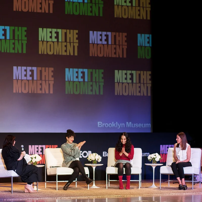 Four people sitting on a stage with a “Meet the Moment” backdrop